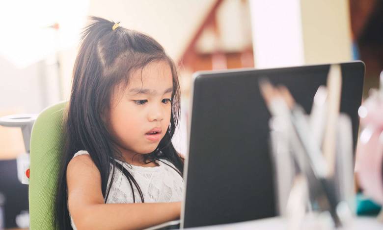 A young girl works on a school assignment on a laptop.