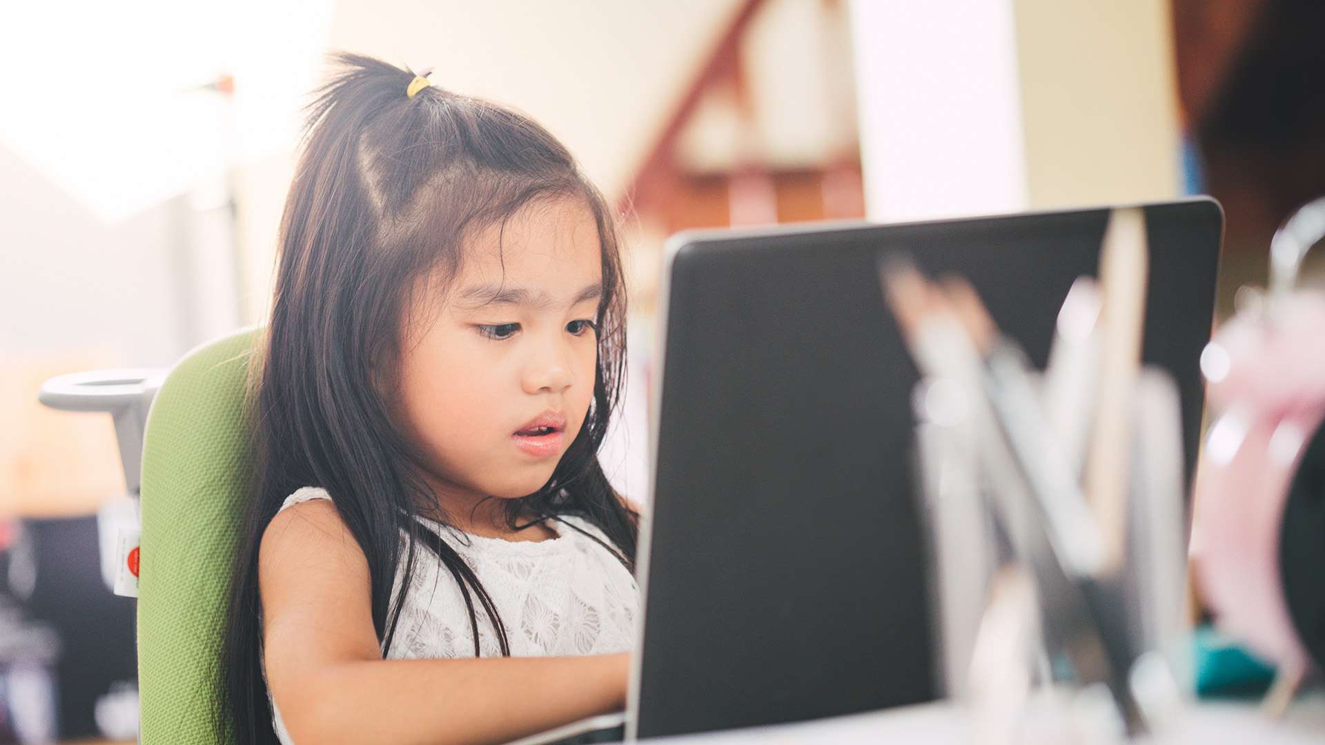 A young girl works on a school assignment on a laptop.