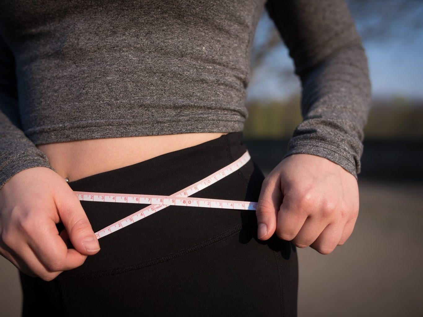 Woman measuring her waistline with a tape measure