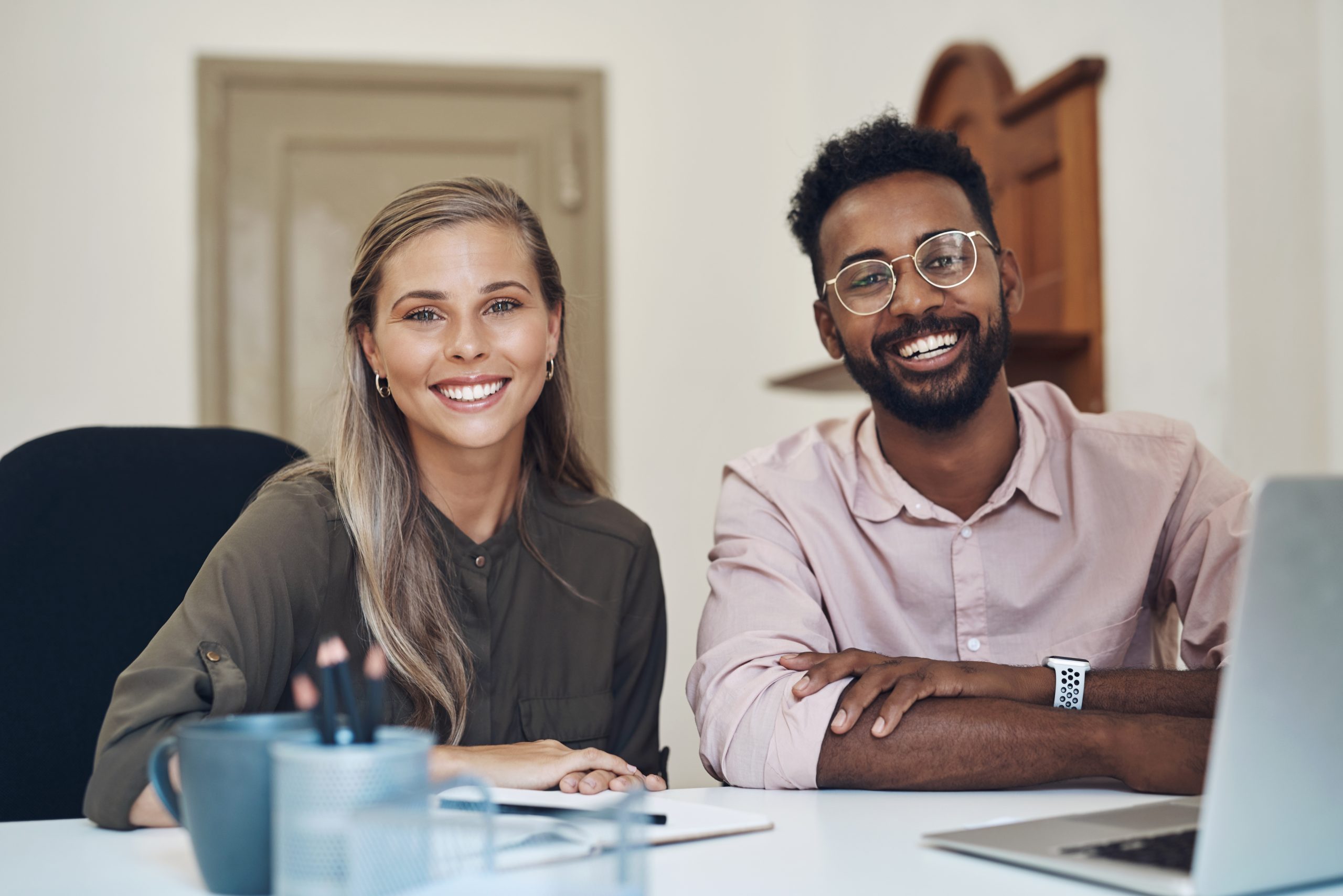A man and a woman in a workspace smiling at the camera - Getting Through Unemployment